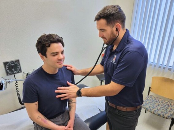 Doctor using stethoscope on male student