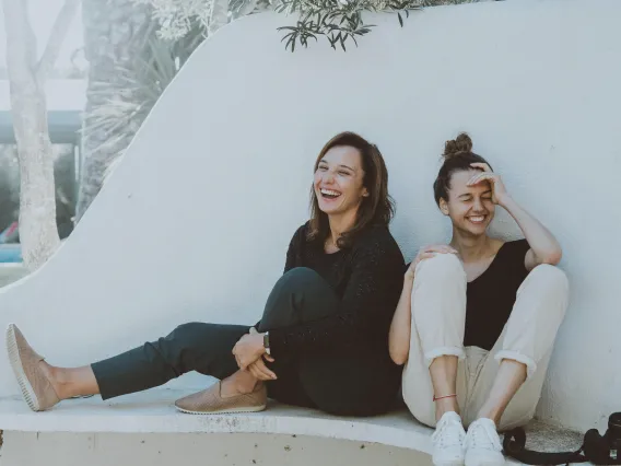 2 female students laughing together on bench