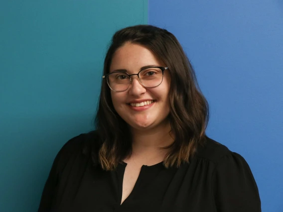 Girl with short brown hair, glasses, smiling with blue green background.