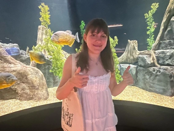 Person with two thumbs up with fish aquarium in the background. 