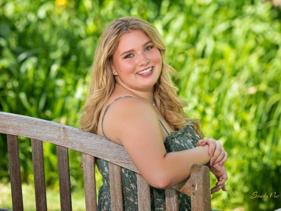 Person with long blonde hair, blue eyes, and green dress with flowers smiling.  