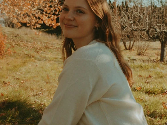 Person with a shirt smiling with autumn trees in the background. 