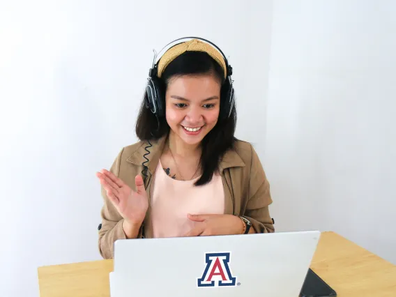 Woman with headphones waiving at computer screen