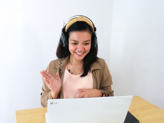 Woman in headphones waiving at computer screen