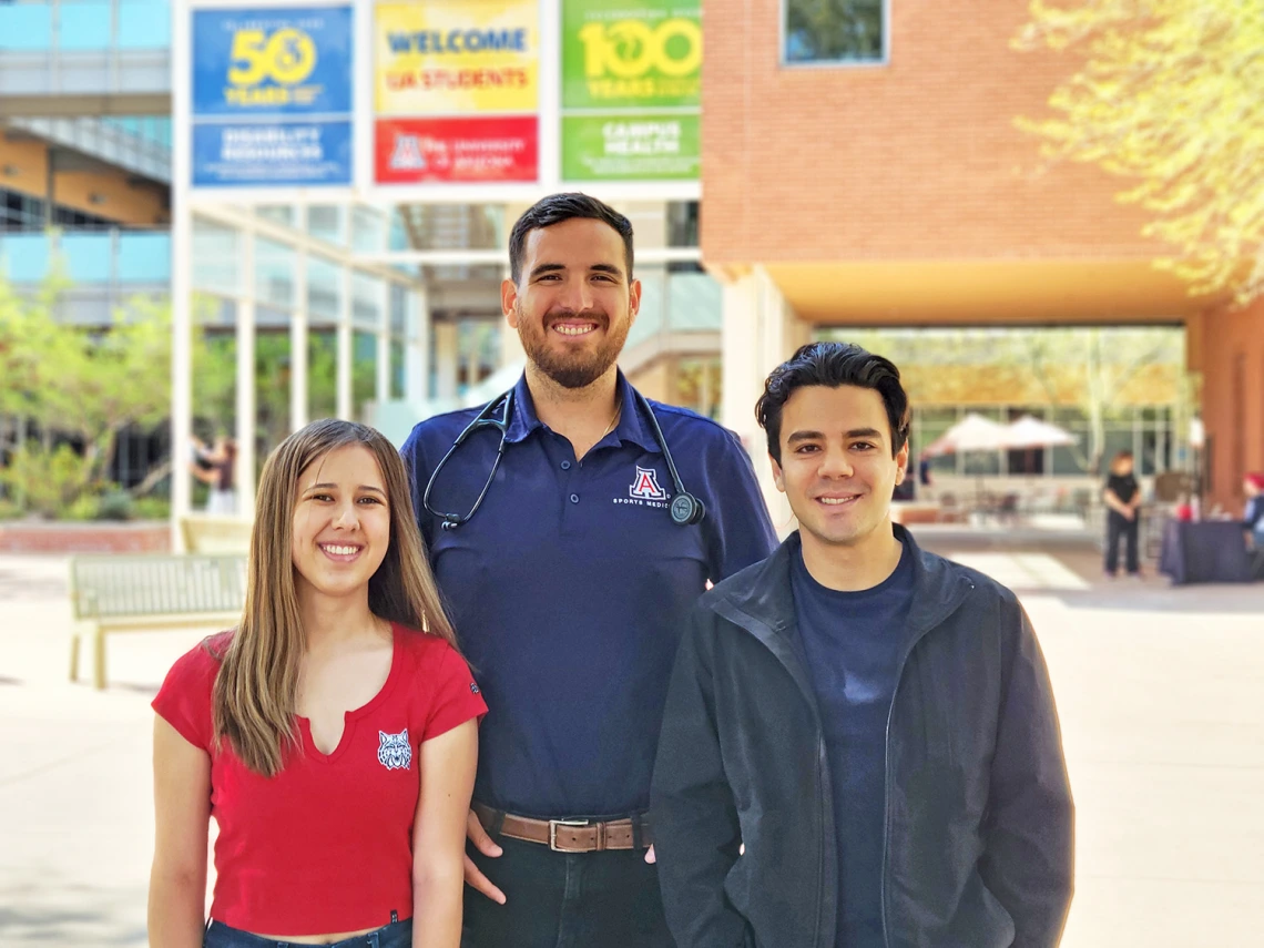 Doctor standing with a male and female student in front of Campus Health