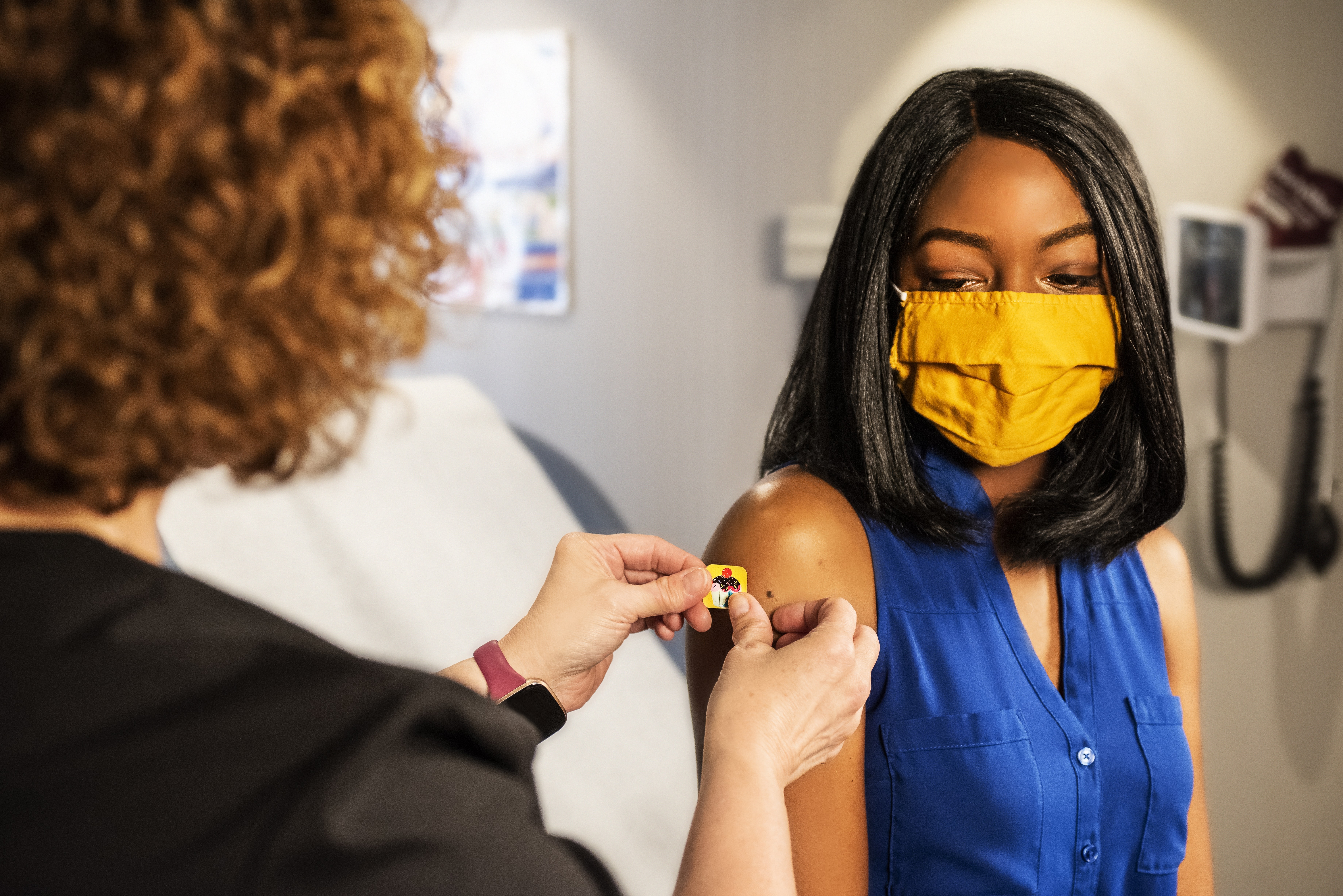 person in doctors office having band aide put on by clinician on arm